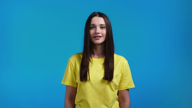 Woman showing yes sure sign, nods her head approvingly. Young lady in yellow t-shirt, body language concept. Blue studio background.