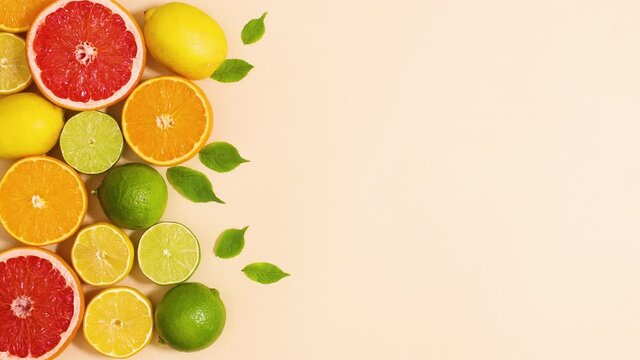 Fresh organic citrus fruits with green leaves move on left side of sandy background. Stop motion flat lay