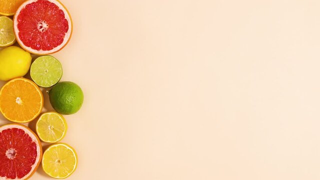 Fresh organic citrus fruits with green leaves ordering on left side of sandy background. Stop motion flat lay