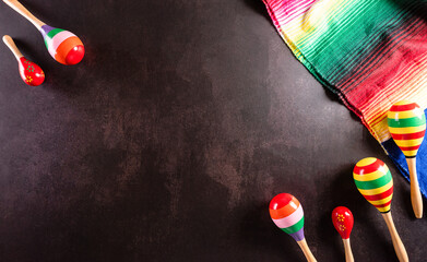 Cinco de Mayo holiday background made from maracas, mexican blanket stripes or poncho serape on dark stone background.