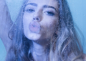 Sexy woman in bodysuit in blue studio kiss over wet glass.