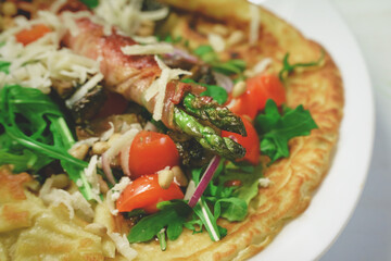 Mediterranean seaseonal meal of pancake with fried asparagus wrapped with bacon garnated with arugula, parmesan cheese, tomato and pine nuts