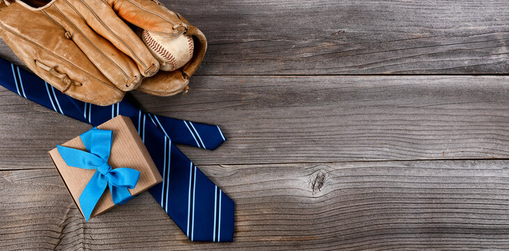 Fathers day concept with blue dress tie, baseball items and a giftbox on rustic wooden background