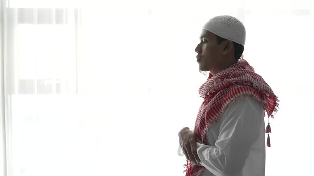 portrait of muslim man using hand to pray against white window