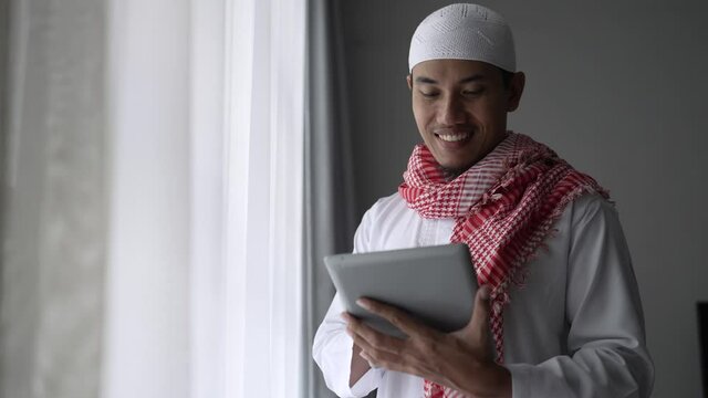 happy muslim businessman smiling while using tablet pc near window