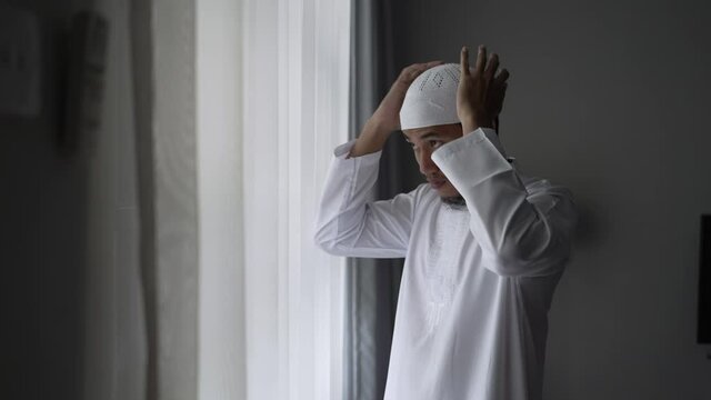 happy muslim asian man standing near window get dressed before going to the mosque