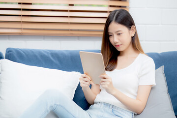 Young attractive asian woman resting using browsing tablet computer on sofa at home, happy girl sitting on couch relax reading digital gadget at house, communication and lifestyle concept.