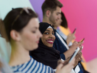 diverse teenagers use mobile devices while posing for a studio photo in front of a pink background