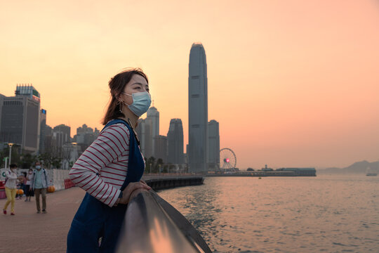 Asian Young Lady With Face Mask, Colorful Magnificent Sunset City View Of Central, Victoria Harbour, Hong Kong In Background