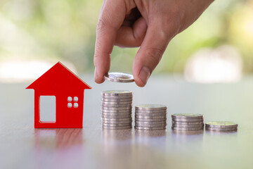 Hand putting money coin stack with small house, purchase of habitation, buy a house,Risk, Assets, Property Investment, Saving money for property investment concept.