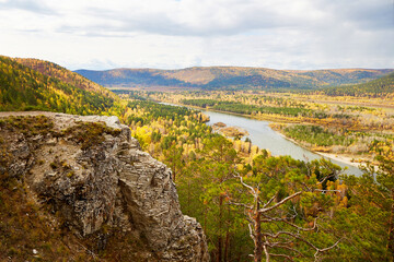 Fototapeta na wymiar Beautiful view from the cliff to the rocks, river, forest. Autumn landscape, trees with yellow leaves, gloomy sky.