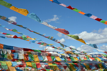 Brightly coloured prayer flags fluttering against a blue sky with white fluffy clouds