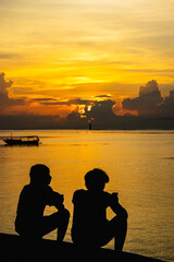 silhouette of a couple sitting on a pier enjoying the sunset