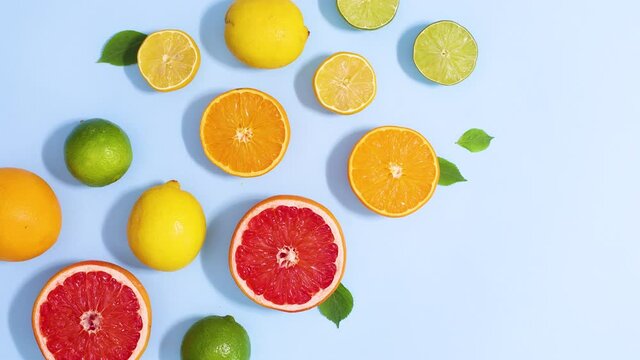 Sliced citrus grapefruit, lemons, orange and limes move on bright blue background. Stop motion flat lay