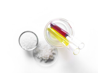 Microcrystalline wax in glass container, Flake salt in Chemical Watch Glass, Potassium Permanganate and Nickle chloride liquid in test tube. Cosmetic chemicals ingredient on laboratory table. Top view