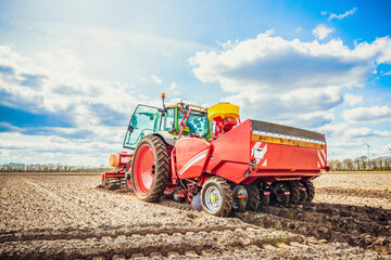 Large, green, modern tractor from Germany sowing potatoes in the field on a sunny spring day