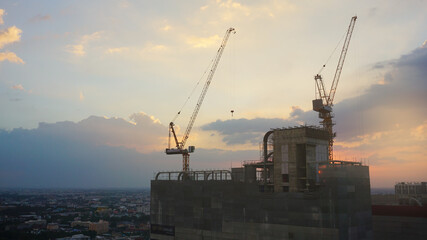 Cranes and high-rise buildings construction site on sunset sky background.