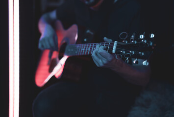 Close up of a guitarist playing an acoustic guitar in a dark room.