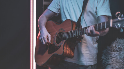 Close up of a guitarist playing an acoustic guitar in a dark room. - obrazy, fototapety, plakaty