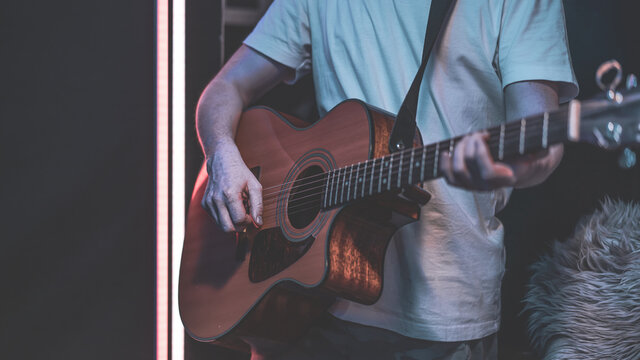 Close up of a guitarist playing an acoustic guitar in a dark room.