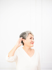 Senior asian woman smiling with hand over ear listening an hearing to rumor or gossip.