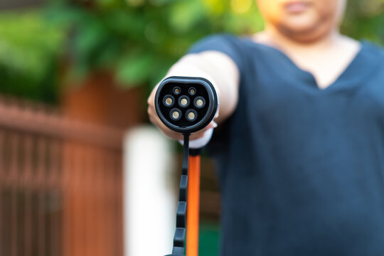 Close up electric car plug on woman hand for recharge plug in hybrid car at home or charging station. World Environment Day. save world save life concept.