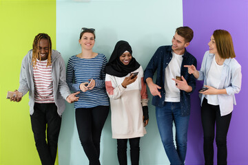 diverse teenagers use mobile devices while posing for a studio photo in front of a pink background