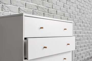 Modern chest of drawers on brick background, closeup