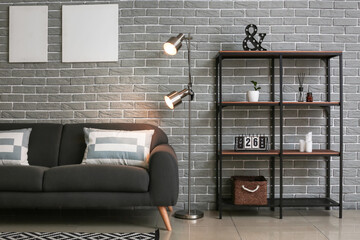 Glowing lamps, sofa and shelf unit near brick wall in room