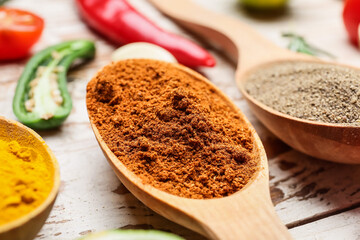 Spoons with different spices on light wooden background, closeup