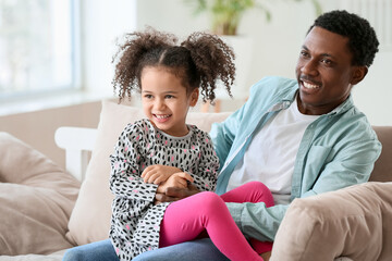Portrait of happy African-American father and his little daughter at home