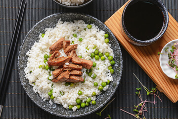 Plate with tasty rice, green peas and meat on dark background