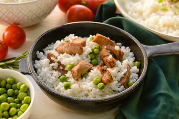 Frying pan with tasty rice, meat and green peas on light background, closeup