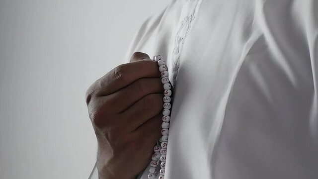 muslim man dhikr using tasbeeh prayer beads or misbaha (with repetitive Arabic text that reads Allah, Muhammad Prophet on the beads)