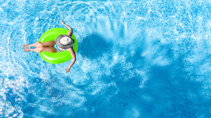 Active young girl in swimming pool aerial top view from above, child relaxes and swims on inflatable ring donut and has fun in water on family vacation, tropical holiday resort
