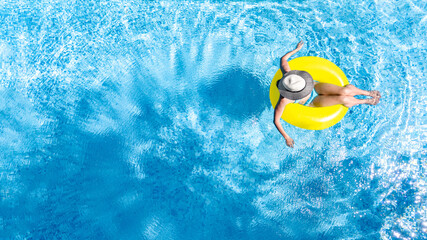 Active young girl in swimming pool aerial top view from above, child relaxes and swims on inflatable ring donut and has fun in water on family vacation, tropical holiday resort
