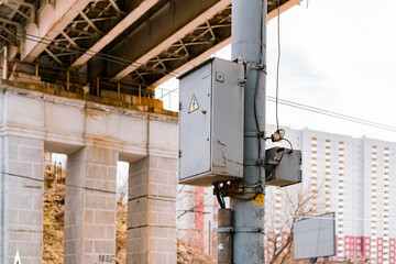 Electric box with wires installed on grey pole in the city. Tall building on the background. Lightning warning signage. Dangerous. Danger. Electricity. Outdoor. Urban