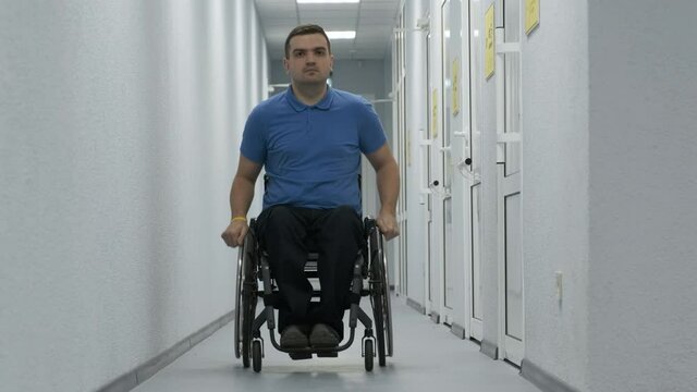 A man in a wheelchair drives down the hallway. A person with a disability moves around the hospital.
