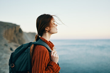 woman tourist with a backpack in a sweater are resting in the mountains near the sea and looking at the sky