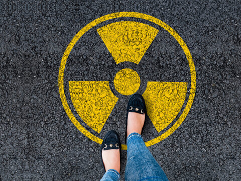 legs in shoes standing on asphalt road and radioactive sign
