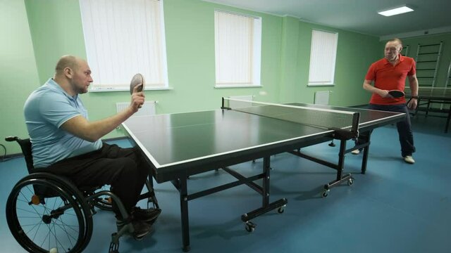 A man in a wheelchair plays ping pong. People with disabilities play table tennis. Rehabilitation of the disabled. Paralympic sport.