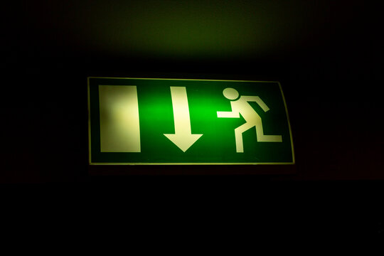 green sign indicating fire exit, arrow down straight exit on black background.