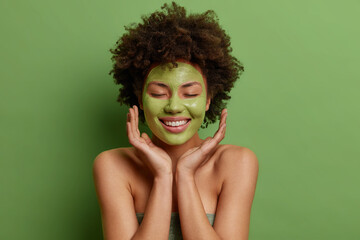 Skin care and beauty treatments concept. Pleased Afro American woman touches face gently applies...