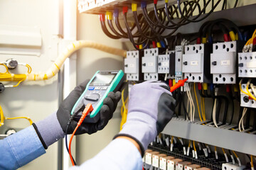 Electrical engineer using digital multi-meter measuring equipment to checking electric current voltage at circuit breaker and cable wiring system in main power distribution board.