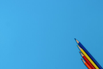 Four colored pencils on a blue background. View from above.