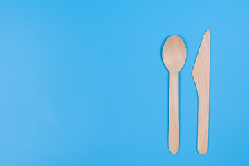 Disposable spoon and knife made of wood on a blue background.