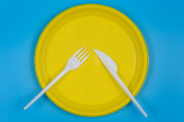 Disposable plate, knife and fork on a blue background.