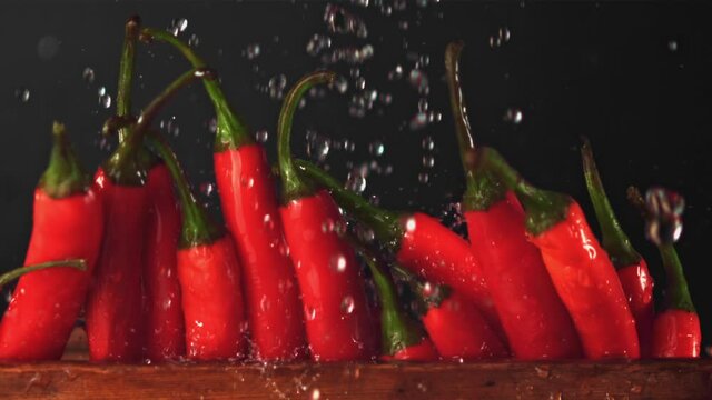 Super slow motion on pods of red chilli pepper in a row drops water. On a black background. Filmed on a high-speed camera at 1000 fps. High quality FullHD footage