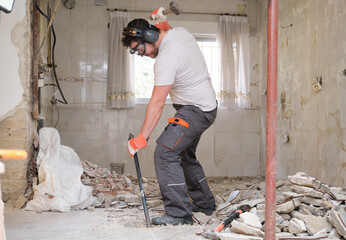Construction worker digging up the house floor, lifting up old tiles with a crowbar and a hammer....