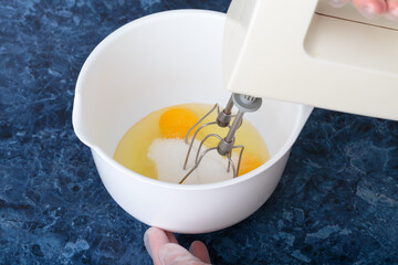 A blender whips eggs and sugar in a bowl.